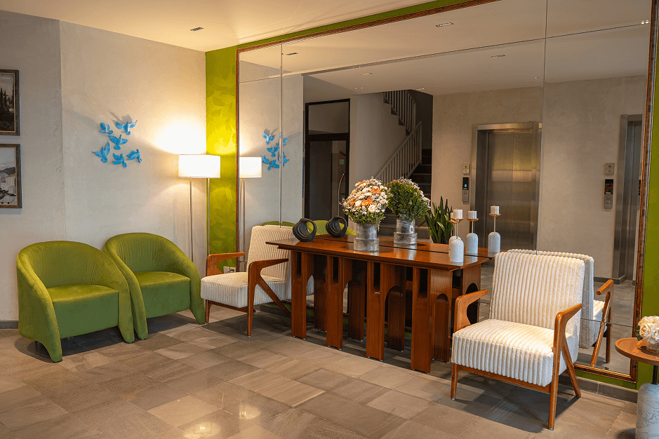Cyrus One lobby seating area with green and cream armchairs, a wooden console table, fresh flowers, and a mirrored wall in Islamabad.