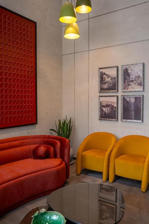 Lounge seating area at Cyrus One with a curved rust-colored sofa, mustard armchairs, and framed artwork, part of the hotel's interiors.
