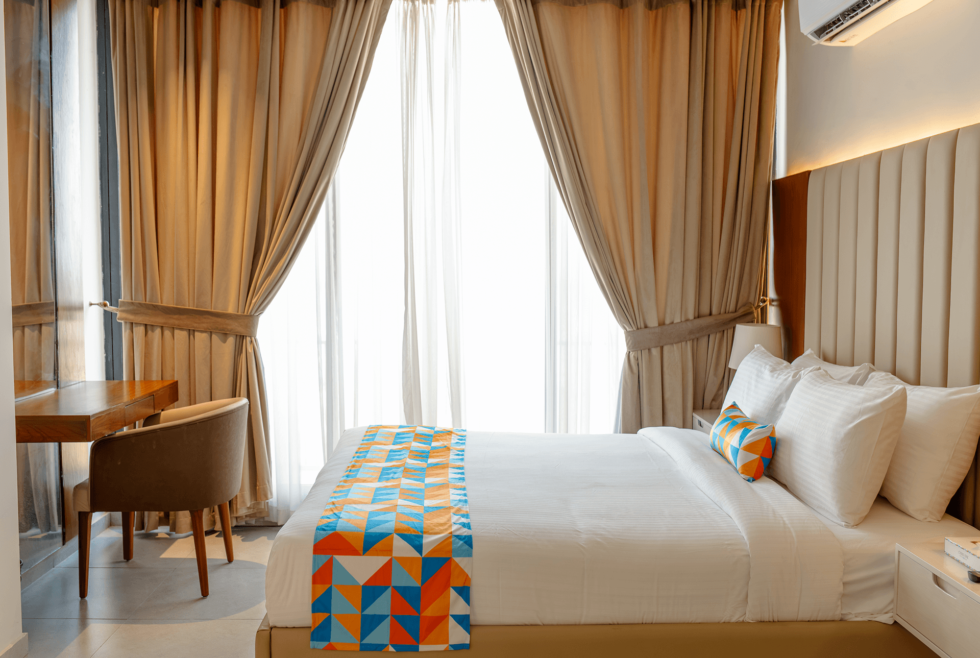 Curtained bedroom window with a colorful geometric bed runner, the background photo behind Cyrus One's room features section, Islamabad.