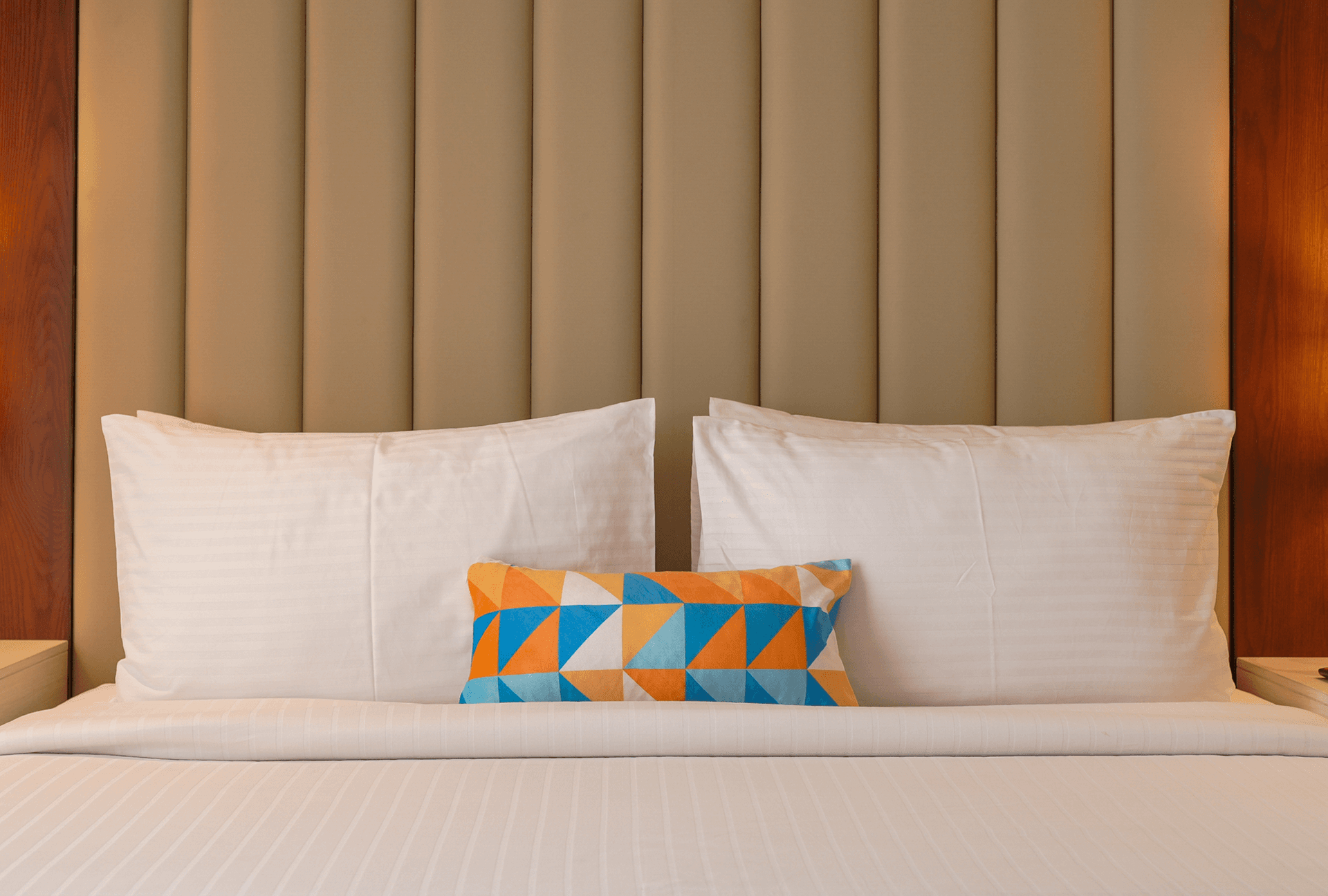 Hero section showing a comfortable hotel bed with white pillows and a colourful accent cushion in a Cyrus One room.